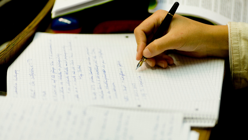 Eine Person schreibt etwas mit einem Füller auf kariertes Papier.