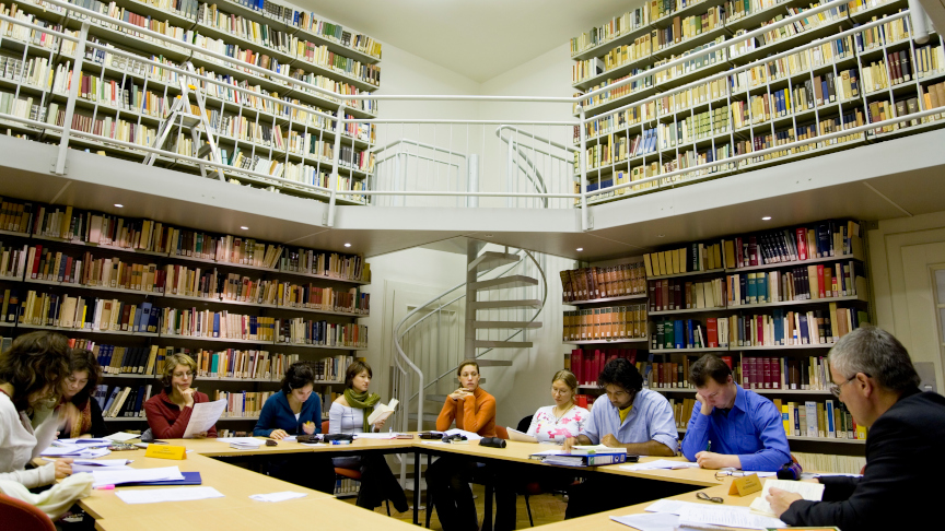 Several people are sitting in a seminar in a library.
